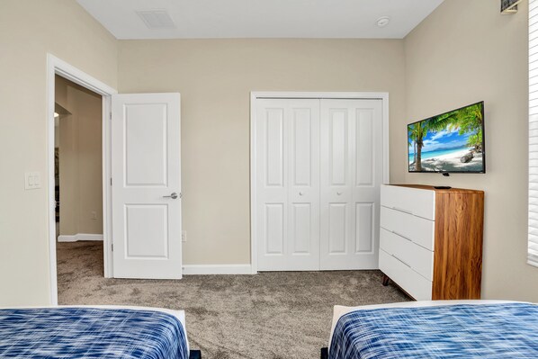 A bedroom with two beds, a white wardrobe, a television on the wall, and a door leading to another room.