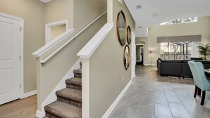 A spacious living area with a staircase, a dark-colored sofa, and a light blue chair. - Bookmark Storey Lake Villa 8 (Kissimmee)