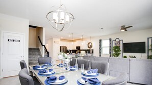A dining area with a table set for six, a grey sofa, and a staircase leading to another level.