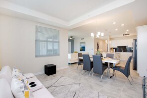 A modern living room with a sofa, dining table, and chairs. There is a kitchen area with cabinets and a refrigerator. - Paradox Condo Story Lake (Kissimmee)