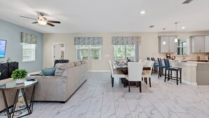 Ein modernes Wohnzimmer mit Sofa, Esstisch und Stühlen, eine Küche mit Schränken und einer Arbeitsplatte sowie ein Deckenventilator.