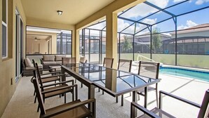 A spacious indoor area with a glass table and chairs, large windows, and a view of a swimming pool. - Misty Villa Solterra 5 (Davenport)