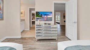 Une chambre d’hôtel dotée d’un grand téléviseur à écran plat, d’une commode moderne et offrant une vue sur la plage par la porte ouverte.