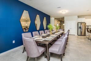 A dining area with a long table set for a meal, surrounded by chairs, and a kitchen in the background.