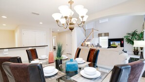 A dining area with a glass table, chairs, and a chandelier. There is a staircase leading to an upper level. - Victoria Villa Porvidence 8 (Davenport)