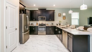 A modern kitchen with dark cabinets, stainless steel appliances, and a marble floor. - Bookmark Villa Story Lake 3 (Kissimmee)
