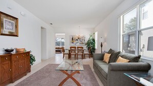 A modern living room with a glass coffee table, grey sofa, wooden cabinet, and a dining area with chairs and a table. - Pine Villa Winwood Bay (Davenport)