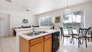 A modern kitchen with a large island, double sink, and a dining area with chairs and a table. - Pine Villa Winwood Bay (Davenport)