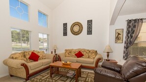 Ein Wohnzimmer mit zwei Sofas, einem Couchtisch und einem braunen Ledersessel. An den Wänden hängen zwei Wanduhren und ein gerahmtes Bild.
