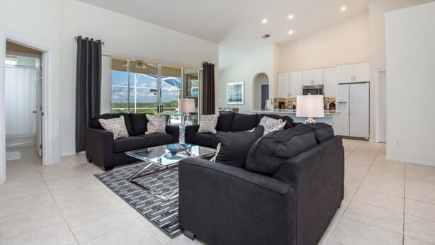 A modern living room with a black sofa set, a glass coffee table, and a view of the outdoors. - Belfry Drive Villa Highlands Reserve 4 (Davenport)