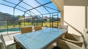A glass-enclosed patio with a table and wicker chairs, overlooking a swimming pool and a landscaped area. - Victoria Villa Porvidence 4 (Davenport)