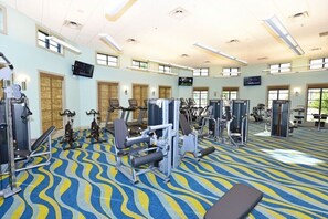 A gym with various exercise machines, a patterned carpet, and large windows allowing natural light. - Drop Shot Villa Champions Gate (Kissimmee)