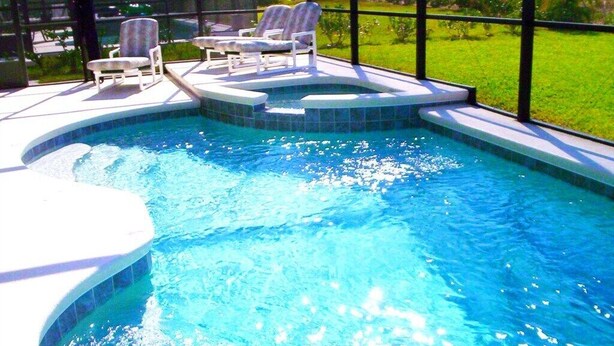 Piscina com hidromassagem, cercada por espreguiçadeiras, e vista para uma paisagem verde.