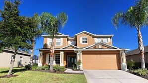 A two-story house with a garage, surrounded by well-maintained lawns and palm trees.