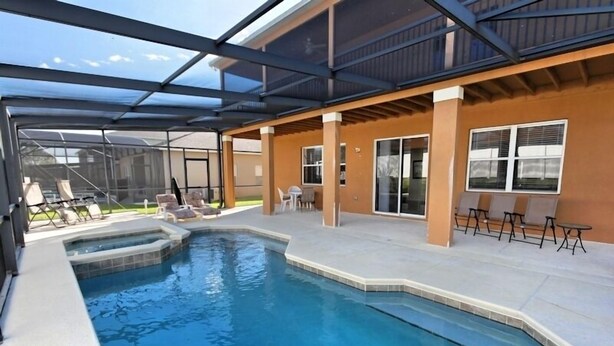 A pool area with a glass enclosure, lounge chairs, and a patio with tables.