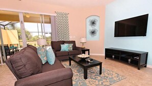A living room with a brown sofa, a coffee table, and a TV on a stand. - Terrasonnesta Drive Villa Solterra 4631 (Davenport)