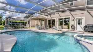 Ein Schwimmbecken mit überdachter Terrasse, Liegestühlen und einem Whirlpool.