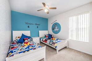Habitación infantil con dos camas, un ventilador de techo y una ventana con persianas.