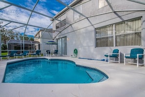 A swimming pool with a covered area, lounge chairs, and a hose reel.