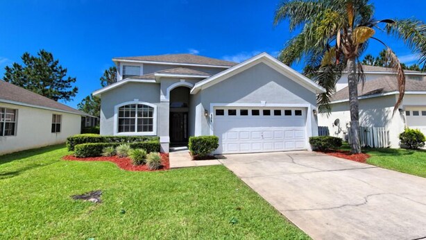 A two-story house with a garage, a well-maintained lawn, and a palm tree. - Oxford Drive Villa Highlands Reserve (Davenport)