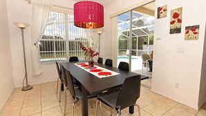 A dining area with a dark wooden table, six chairs, a red pendant light, and a window with white curtains. - Northampton Drive Villa Highlands Reserve 1812 (Davenport)