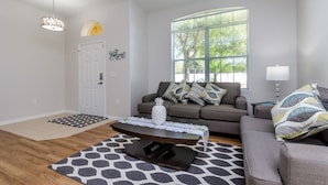A modern living room with a sofa, coffee table, and a large window providing natural light. - Adulusiia Loop Villa Mabella (Davenport)
