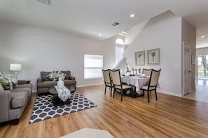 A spacious living room with a dining area, wooden flooring, and a staircase leading to an upper level. - Adulusiia Loop Villa Mabella (Davenport)