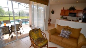 A living room with a sofa, armchair, and coffee table. There is a sliding glass door leading to a patio with a pool and outdoor furniture. - 7783tb Windsor Hills Resort 5 Bed 5 Bath (Kissimmee)