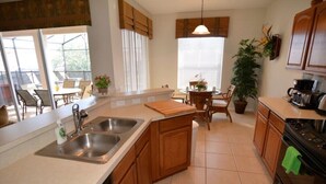 A kitchen with a central island, a dishwasher, a stove, and a dining area with chairs and a table. - 7783tb Windsor Hills Resort 5 Bed 5 Bath (Kissimmee)