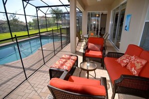A covered outdoor area with a pool, wicker furniture, and a view of the surrounding landscape. - 7783tb Windsor Hills Resort 5 Bed 5 Bath (Kissimmee)