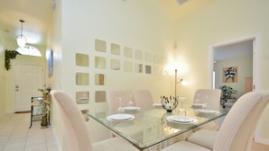 Uma sala de jantar com mesa de vidro, cadeiras brancas e parede decorada com espelhos quadrados.