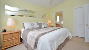 Quarto com cama, mesas de cabeceira, luminárias, ventilador de teto e uma porta.