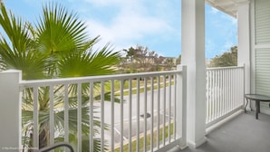 A covered porch with a white railing, a small table, and a view of a street and greenery. - Excitmen t Drive Condo Reunion (Kissimmee)