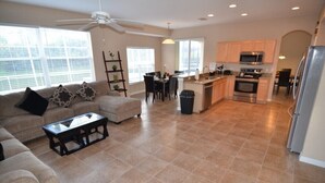 A spacious living room with a sofa and coffee table, a dining area with chairs, and a kitchen with modern appliances. - Bonville Drive Villa Highlands Reserve (Davenport)