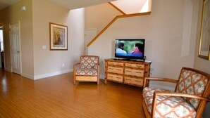 A living room with hardwood flooring, a television, wicker furniture, and a staircase. - 3500cal Stunning Town Home In Regal Plams (Davenport)