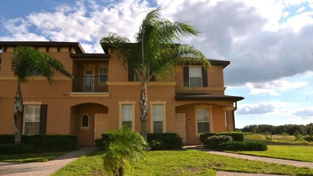A two-story building with a symmetrical facade, a central entrance, and a landscaped front yard with palm trees. - 3500cal Stunning Town Home In Regal Plams (Davenport)