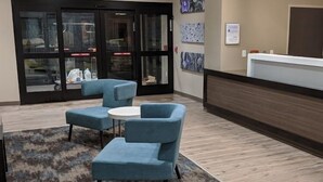 A lobby with a reception desk, blue armchairs, a small round table, and a patterned rug.