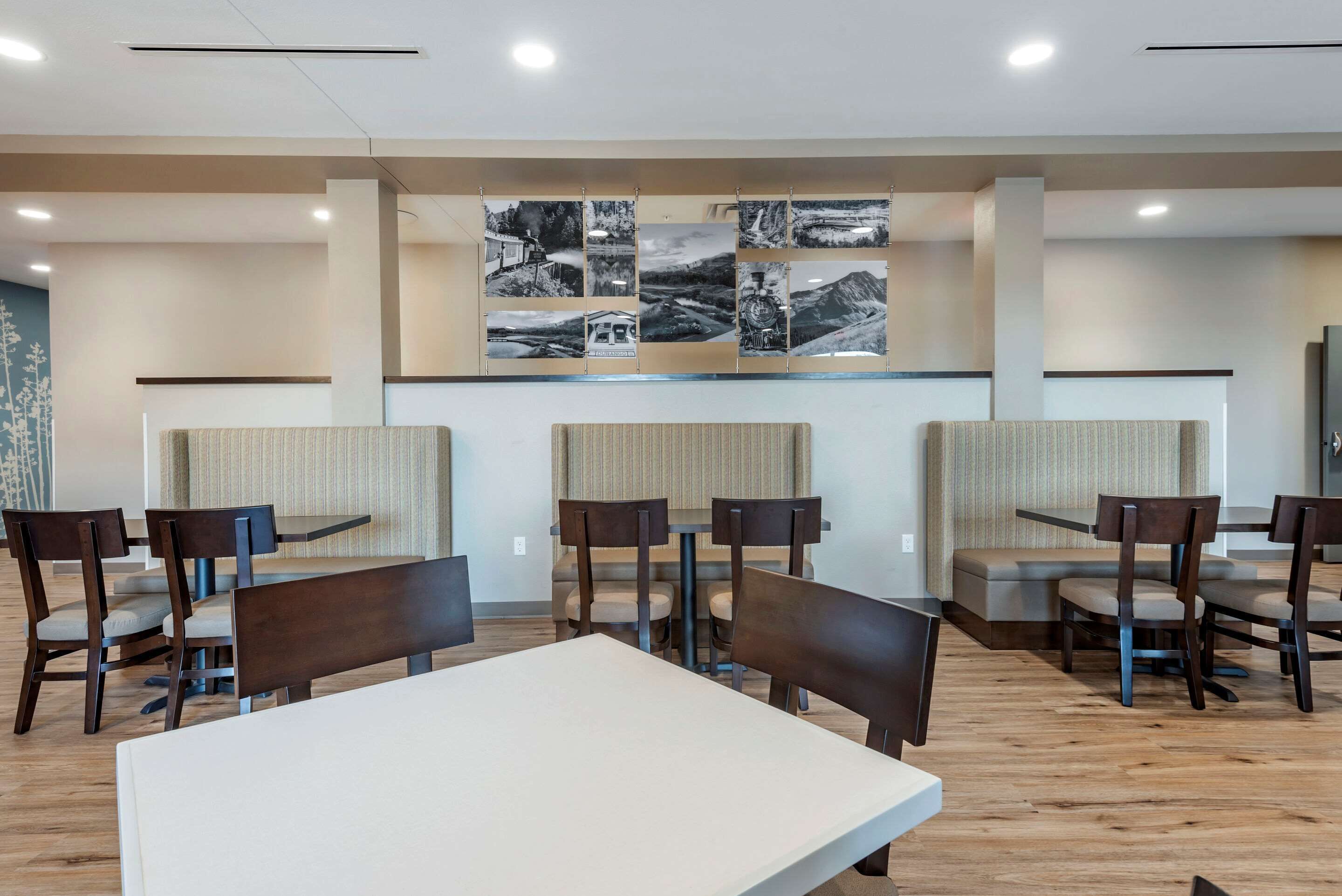A modern dining area with wooden tables and chairs, a central seating area with cushioned benches, and a wall with black and white photographs.