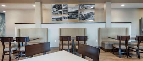 A modern dining area with wooden tables and chairs, a central seating area with cushioned benches, and a wall with black and white photographs.