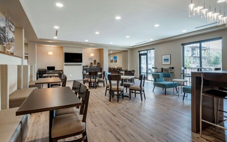 A spacious dining area with multiple tables and chairs, a kitchen area, and large windows providing natural light.