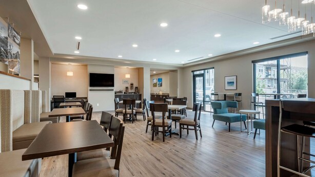 A spacious dining area with multiple tables and chairs, a kitchen area, and large windows providing natural light.