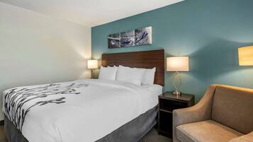 A hotel room with a bed, a nightstand, a lamp, and a sofa.