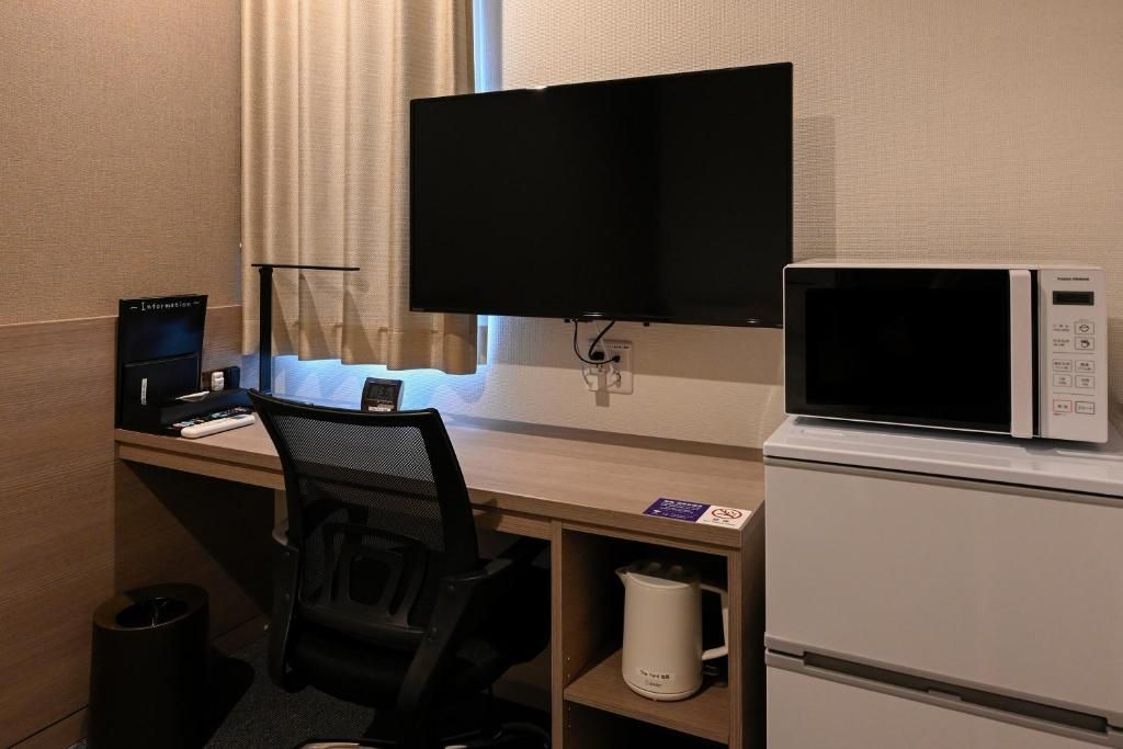 Quarto de hotel com escrivaninha, computador, televisão, micro-ondas e lixeira.