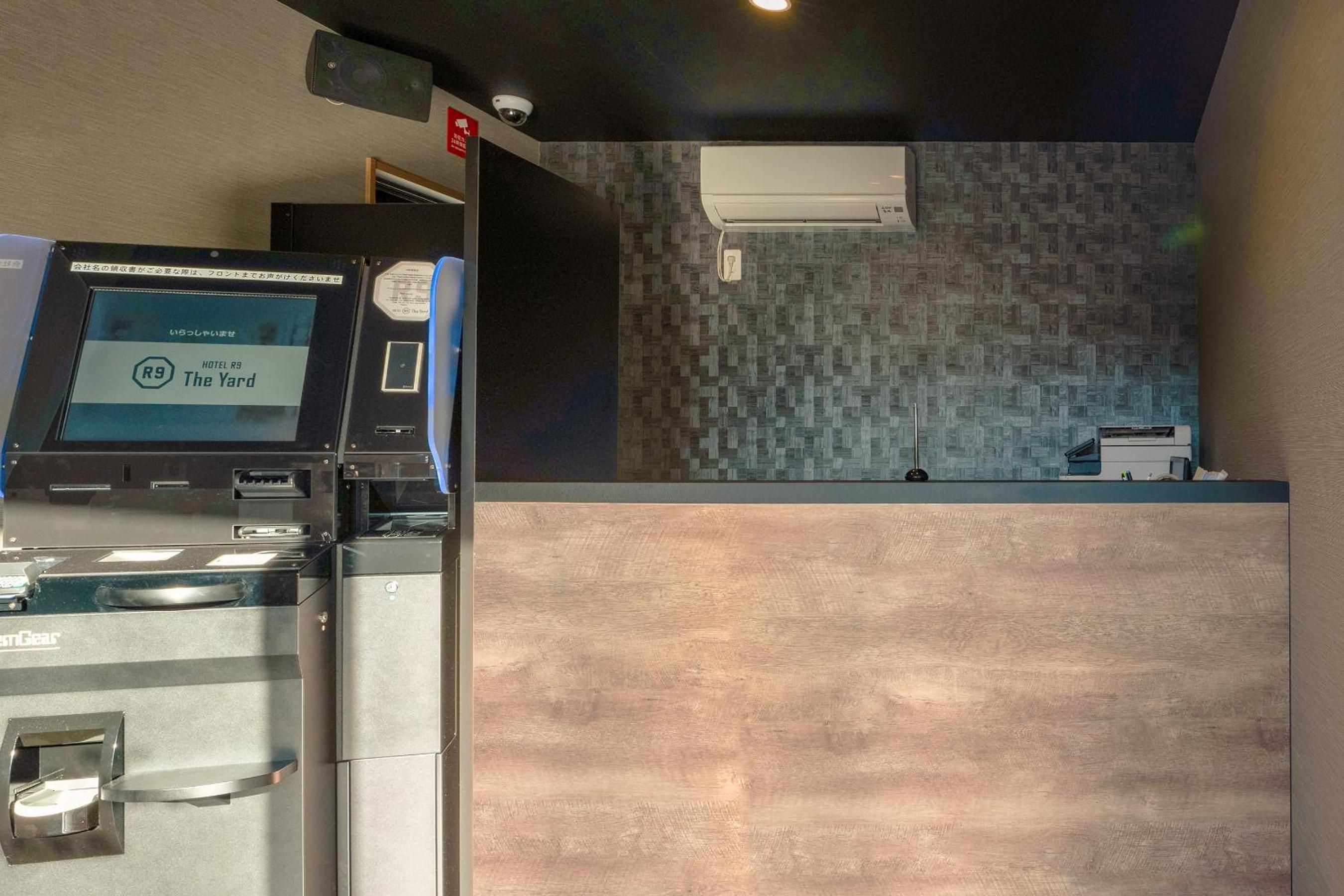Un mostrador de recepción de hotel con una pantalla digital, una cámara de seguridad y un aire acondicionado de pared.