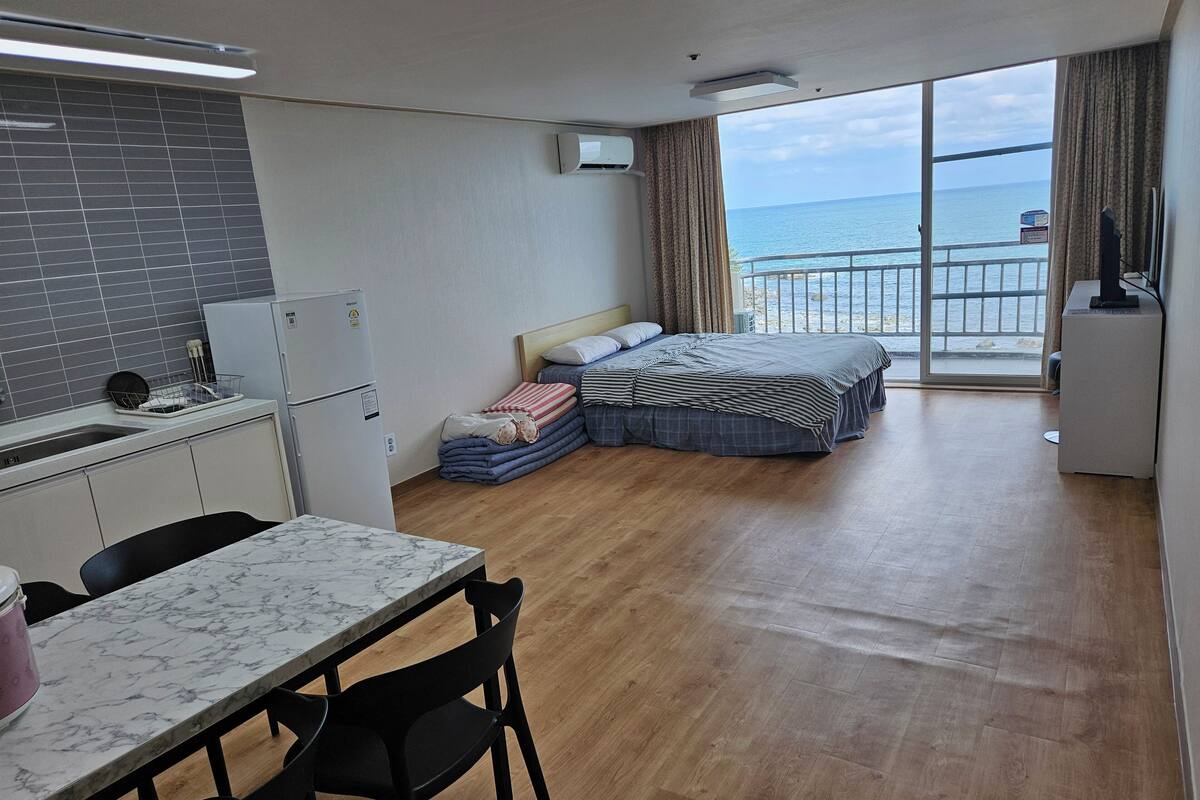 Ein kompaktes Hotelzimmer mit Küchenzeile, einem Bett mit Meerblick und einem Balkon mit Geländer.