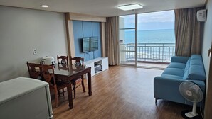 Uma sala ampla com uma mesa de jantar de madeira, sofá azul e uma grande janela com vista para o mar.