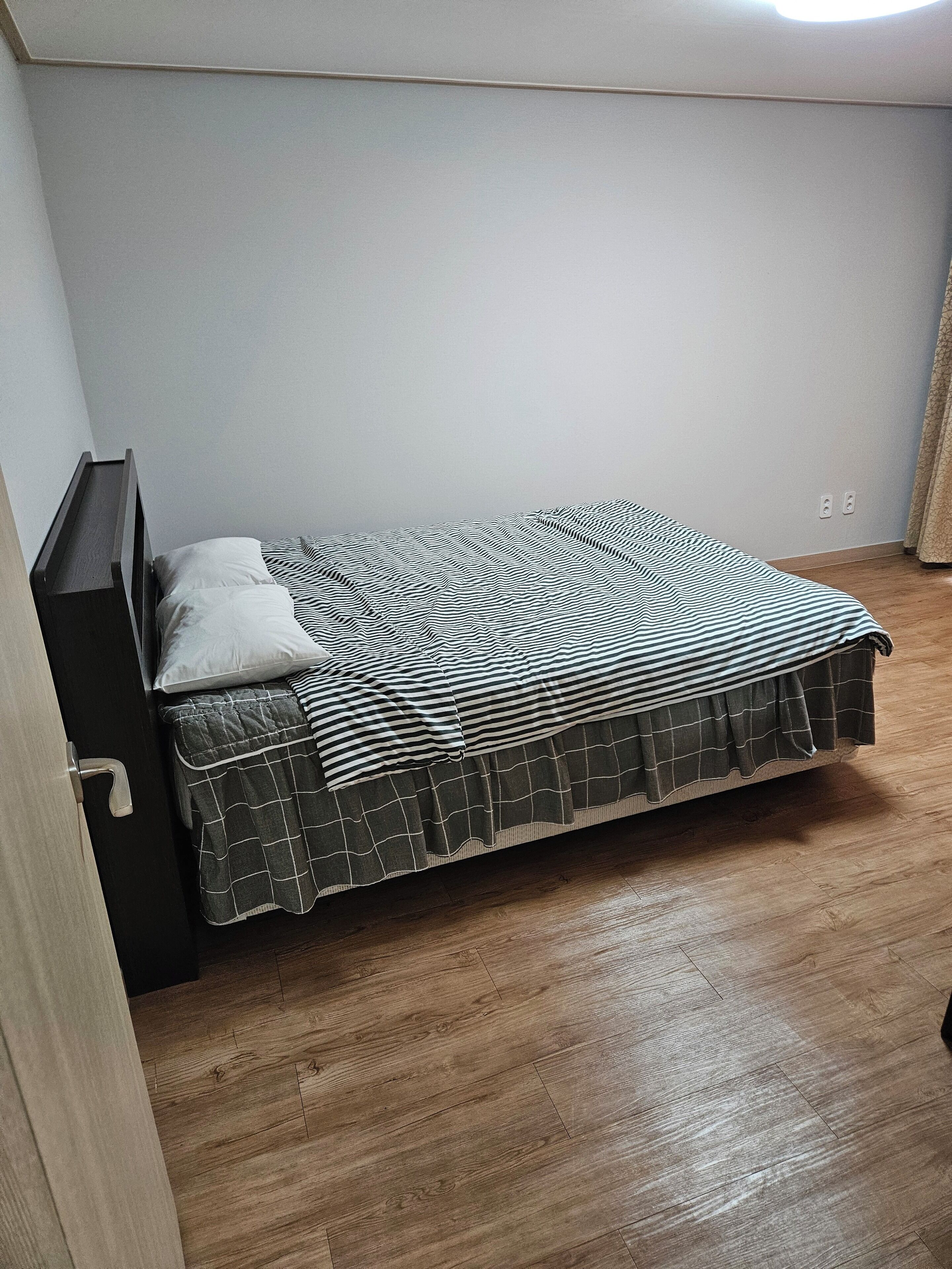 A single bed with a striped bedspread and a quilted blanket, a wooden nightstand, and a wooden floor.