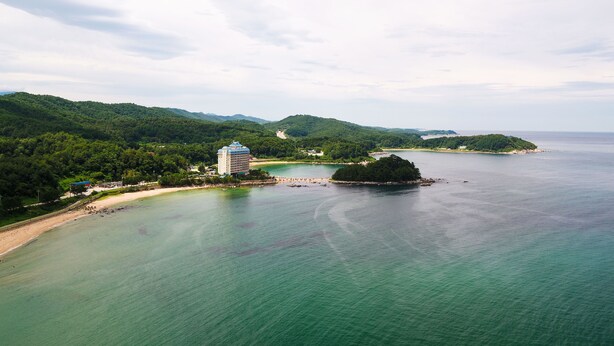 Hotel à beira-mar com um edifício grande, uma praia e uma ilha arborizada ao fundo.
