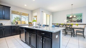 A modern kitchen with dark cabinetry, a granite countertop, and a dining area with a table and chairs. - Family Friendly 4Bd with Pool Solara Resort 1517 (Kissimmee)