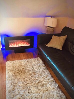 Un salon avec une cheminée, un canapé en cuir noir, un tapis moelleux et une lampe.